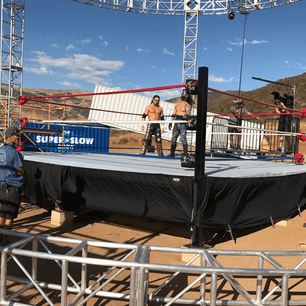 PROLAST 10 x 10 ft boxing ring, 2 ft platform: red-roped ring with a black skirt on an outdoor desert set, two performers inside
