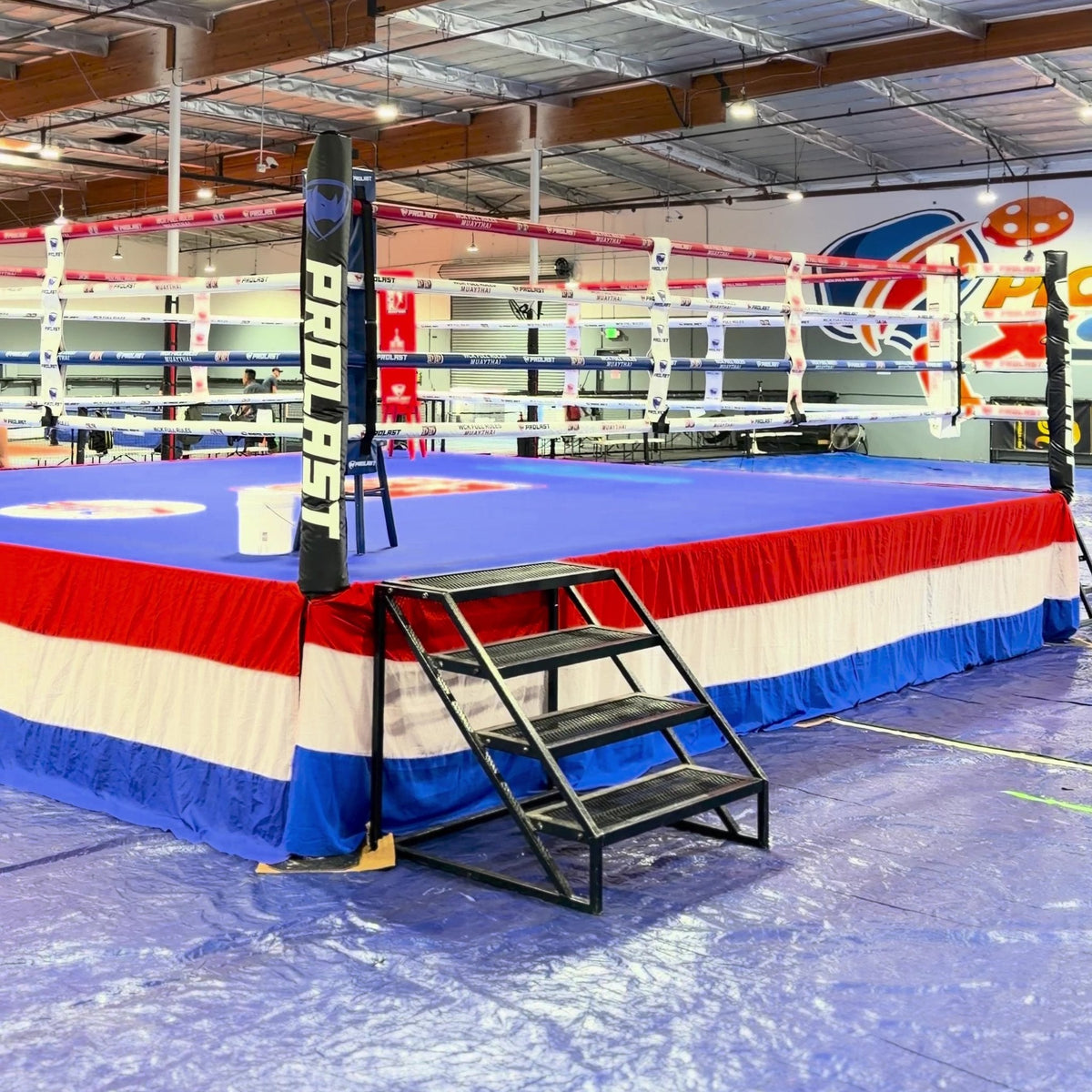 PROLAST boxing ring with a red, white and blue skirt and steel stairs at a Muay Thai event