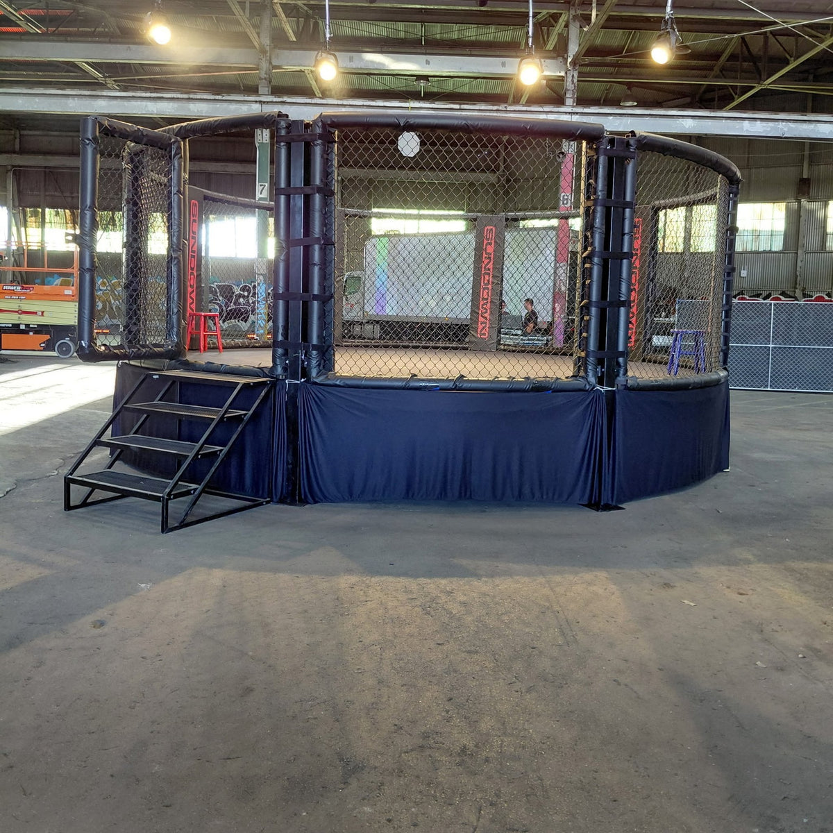 PROLAST MMA cage with a blue skirt and stairs in a warehouse