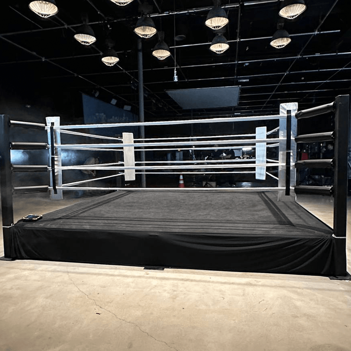 PROLAST 8 x 8 ft boxing ring, 2 ft platform: black ring with white ropes and white corner pads under hanging lights