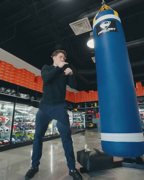 A man punching, then high-kicking, a blue 5 ft PROLAST heavy bag