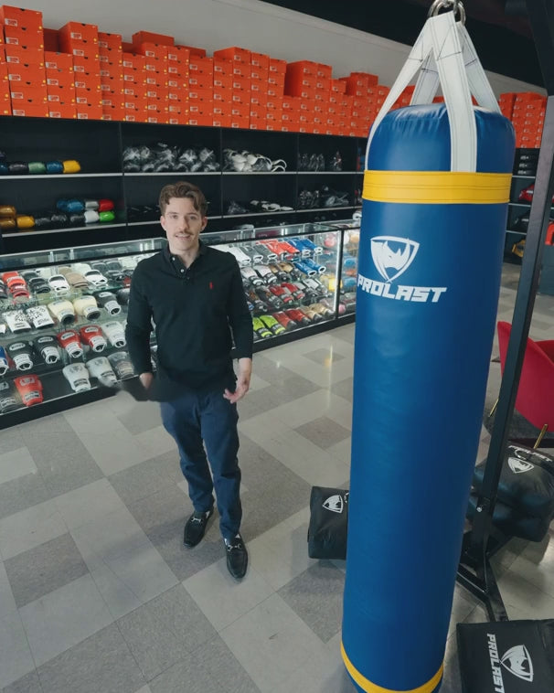 A man standing next to a blue 6 ft PROLAST heavy bag hanging at full length