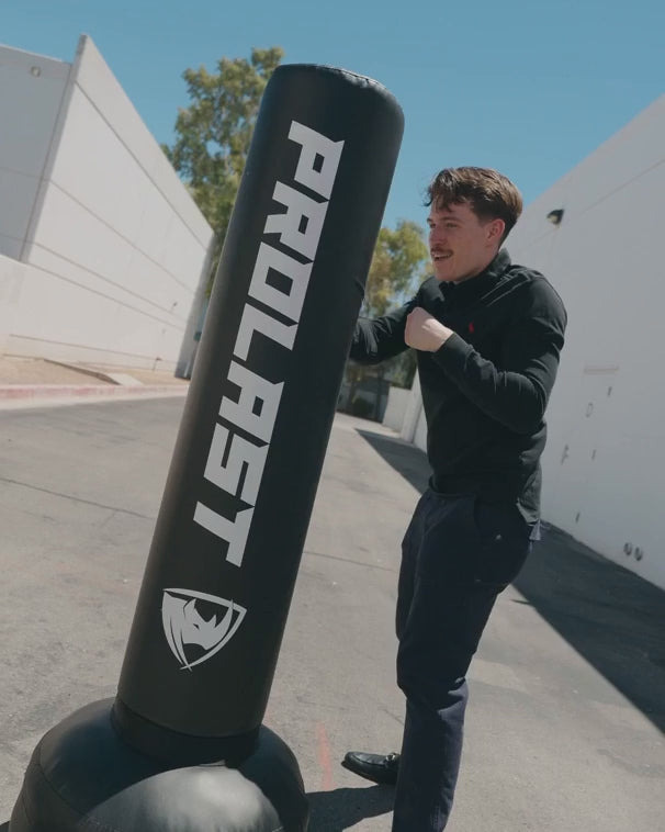 A man punching a black PROLAST freestanding bag outdoors, then pulling on its top