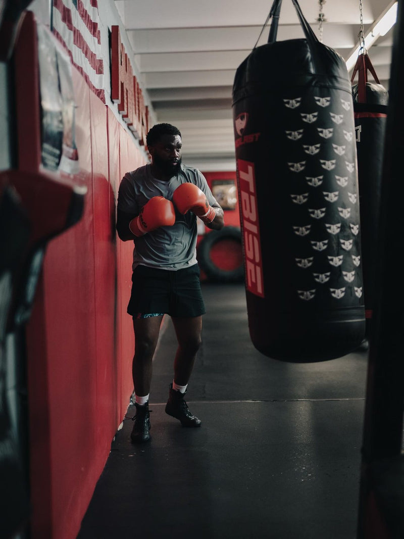 Jaron “Boots” Ennis in his guard beside his custom black TBSE heavy bag, made by PROLAST
