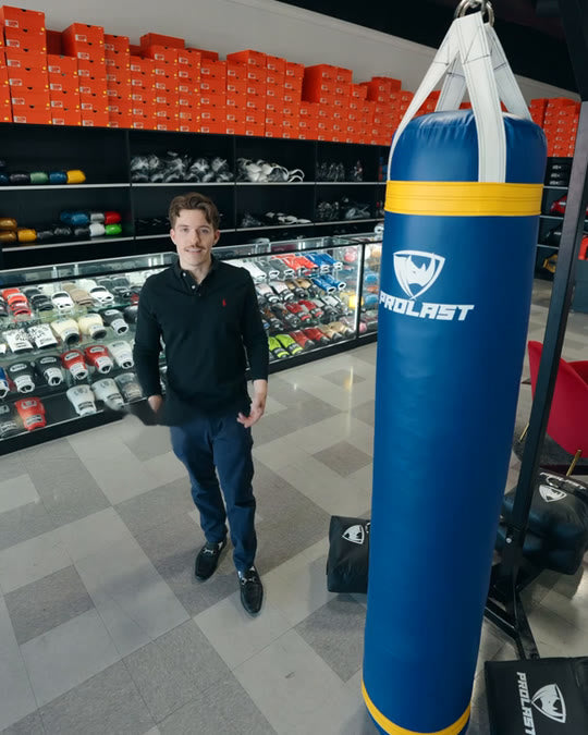 A man standing next to a blue 6ft PROLAST heavy bag hanging at full length